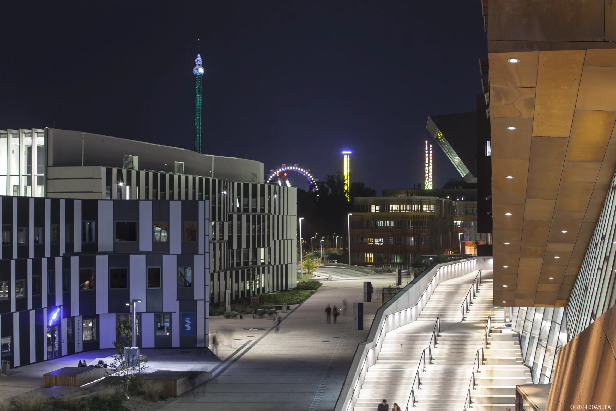Nächtlicher Campus der Wirtschaftsuniversität Wien mit moderner Architektur, beleuchteter Treppe und Blick auf den Prater im Hintergrund.